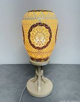 Photo showing lit porcelain lampshade with visible intricate cutout lattice and floral hand painted decorations, displaying warm light glow.