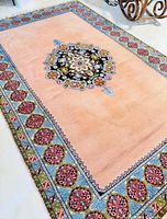 Full view of the vintage hand woven wool rug laid on the floor showing peach background and patterned borders