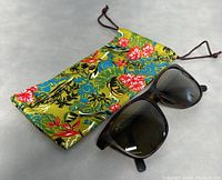 Overview of sunglasses and floral-print drawstring pouch on gray background