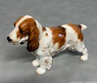 Side view of porcelain dog figurine showing brown and white coloration on glossy surface.