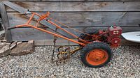 Side view of antique cultivator showing orange frame, large treaded tires, and metal cultivator attachment.