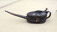 Side angle view of antique black metal oiler can with gold marking, long spout, and handle.
