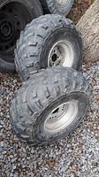 Pair of used ATV tires size 25x12-10 with metal rims, placed outdoors on gravel and dirt.
