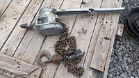 Complete view of come along chain hoist on wooden surface showing lever, chain, and hook.