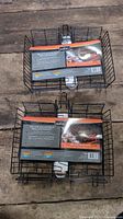 Two brand new deluxe adjustable BBQ grilling baskets stacked on wood surface with packaging labels visible.