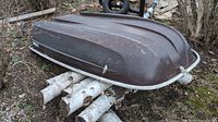Overturned brown fiberglass boat hull resting on birch logs, showing scratches and wear.