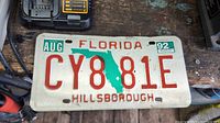 Photo shows a vintage Florida license plate dated 1992 from Hillsborough county with the registration CY8 81E. Plate is white with red letters and a green Florida silhouette in the center.