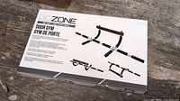 White box of Go Zone Door Gym showing images of the pull-up bar and its use on a door frame, placed on a wooden floor outside.
