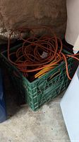 Photo showing a green plastic milk crate filled with orange and yellow power cords and extension cords piled inside.