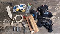 Wide view of entire lot showing knee pads, grip tape rolls, cable, electrical tape, screwdriver, metal wire connectors, wooden sanding block, and more.
