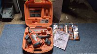 Orange carrying case open showing nailer, batteries, charger