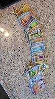 A spread of 43 assorted Pokemon trading cards on a marble countertop in various orientations.
