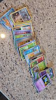 A collection of approximately 40 Pokemon trading cards fanned out on a granite countertop showing a variety of characters, types, and some wear on the cards.
