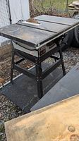 Full view showing the Rockwell table saw with metal stand and worn work surface.