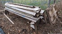 Photo showing stacked lumber planks resting on two wooden stands next to a wooden pallet.