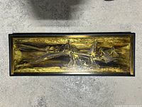 Top-down photo of the rectangular metallic relief wall hanging showing abstract futuristic embossed design with yellow and brown metallic tones.