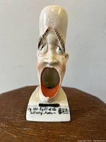 Front view of the porcelain figurine ashtray showing caricatured male figure with open mouth, music note inscription on base