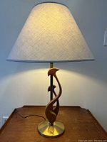 Front view of the lit table lamp showing walnut sculptural base, brass base, and fabric shade