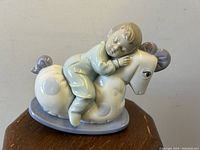 Front view of the porcelain figurine with boy sleeping on rocking horse, placed on wooden table.