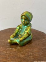 Side/front angle view of small girl child figurine with bright green eosin glaze.