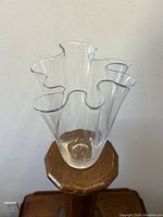 Full view of clear blown Murano glass vase with handkerchief style ruffled top edges, displayed on a wooden stand against a white background.