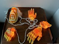 Photo showing the complete set of the vintage Halloween display with illuminated creepy head, two hands, and two feet connected by white wiring on a wooden surface.