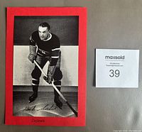 Front view of black and white hockey photo of Babe Siebert adhered to red cardboard backing with handwritten identification.
