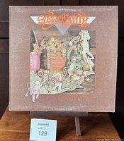 Front cover of Aerosmith LP showing illustrated artwork with band name and album title "Toys in the Attic." Cover has visible surface wear and fading.