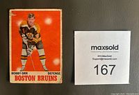 Front of Bobby Orr hockey card showing player in Boston Bruins uniform with red background. Shows moderate wear and edge damage.