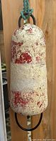 Front view of weathered cylindrical buoy with white and red faded paint showing heavy wear and patina. Attached metal loops at top and bottom visible.