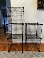 Two stackable black steel wire crates joined vertically and one crate adjacent showing their modular stacking and connection design.