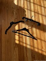 Three types of clothing hangers on wooden floor: one wooden hanger, one plastic shirt hanger, one plastic clip hanger.