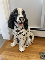 Image of ceramic dog statue positioned on wooden floor next to a baseboard heater and white wall.