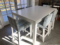 Side view of white dining table with three plaid upholstered chairs placed under window
