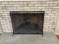 Front view of the black fireplace screen in front of a brick fireplace, showing its mesh screen and metal frame.