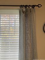Curtain panel hanging on a window with ring clips on a dark metal rod, showing texture and color.
