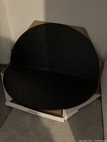 Folded black round table top with a visible seam for folding, placed on the original box