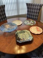 Five serving plates and decorative bowls displayed on a wooden round table with natural light from windows in the background.