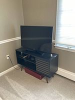 Black TV stand placed in corner with a TV on top showing the storage compartments and overall design.