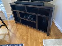 Front and side view of black solid wood corner TV stand showing multiple cubby shelves and angled design fitting a corner.