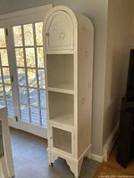 Full view of the white kitchen hutch showing the hand-painted curved top cabinet door, open middle shelves, and screened lower cabinet door.