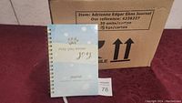 Box of 30 new journals with label 'Adrienne Edgar Enns Journal' and weight info, showing cardboard carton packaging.