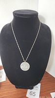 Front view of pendant with 1959 Canadian silver dollar coin and 925 silver chain displayed on black bust.