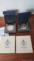 Two silver Canadian Centennial medals in open black leather cases with two white presentation boxes.