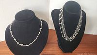 Both 925 sterling silver necklaces shown on black necklace display busts. Left necklace is a single strand with curved bars and bead clusters, right necklace is multi-strand with small silver beads.