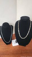 Both necklaces displayed on black necklace busts showing their different chain styles and lengths.