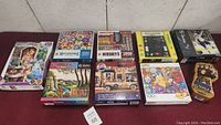 Nine new sealed puzzles arranged in two rows on a table with varied box sizes and colorful artwork.