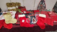 Image showing a variety of Christmas stockings including red plush and gold satin ones, along with multiple boxed red bows and some hanging ornament holders.