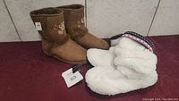 Two pairs of ladies size 9 footwear on red fabric, one pair of brown boots with floral embroidery and white plush slippers with knit patterned trim.