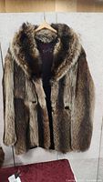 Front view of men's raccoon fur coat on hanger showing fur details and branding inside.